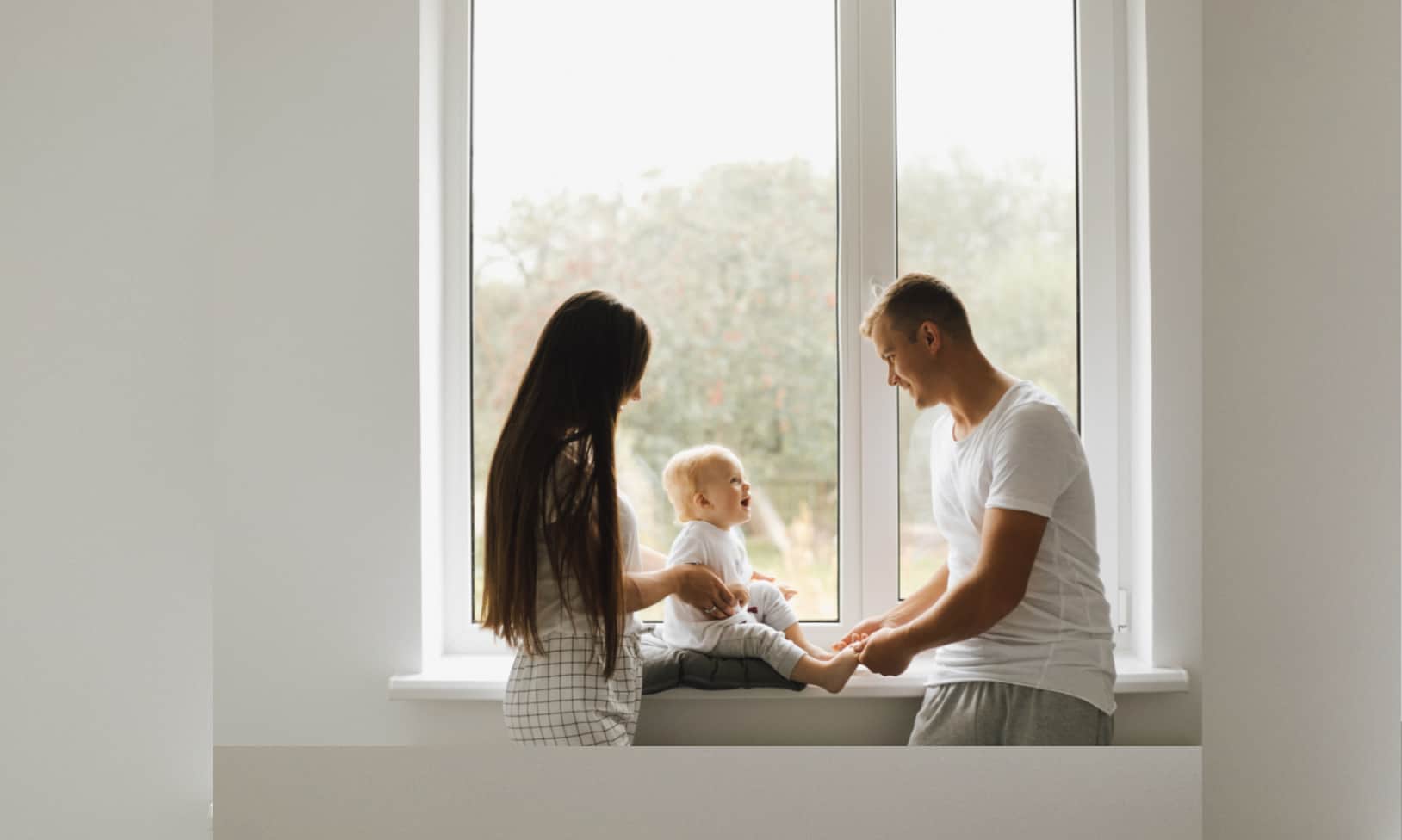 couple with a baby next to a large window in their home, benefiting from the adoption allowance