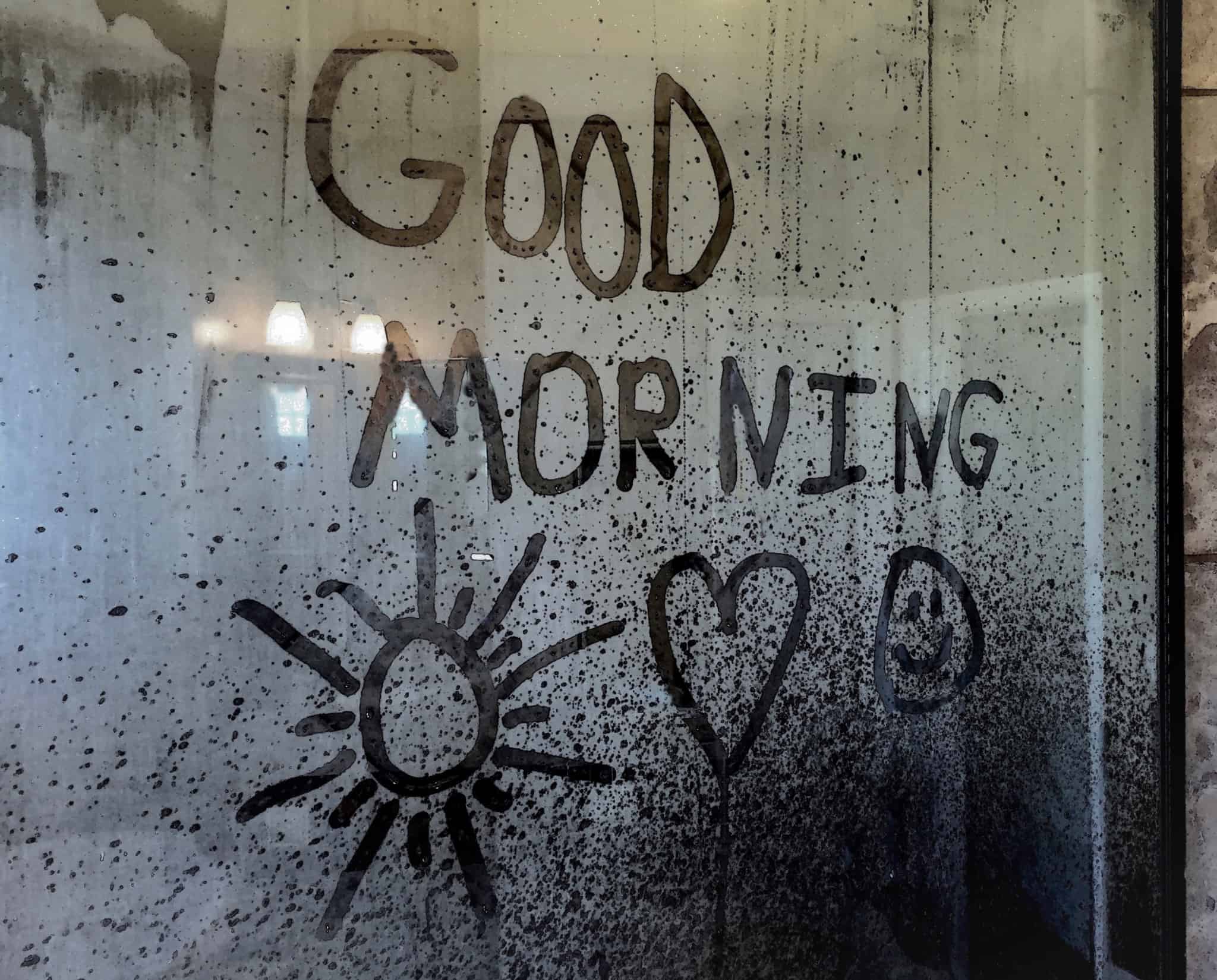 steam from hot water on the bathroom mirror on which the expression good morning and hearts and sun was written by hand and in English