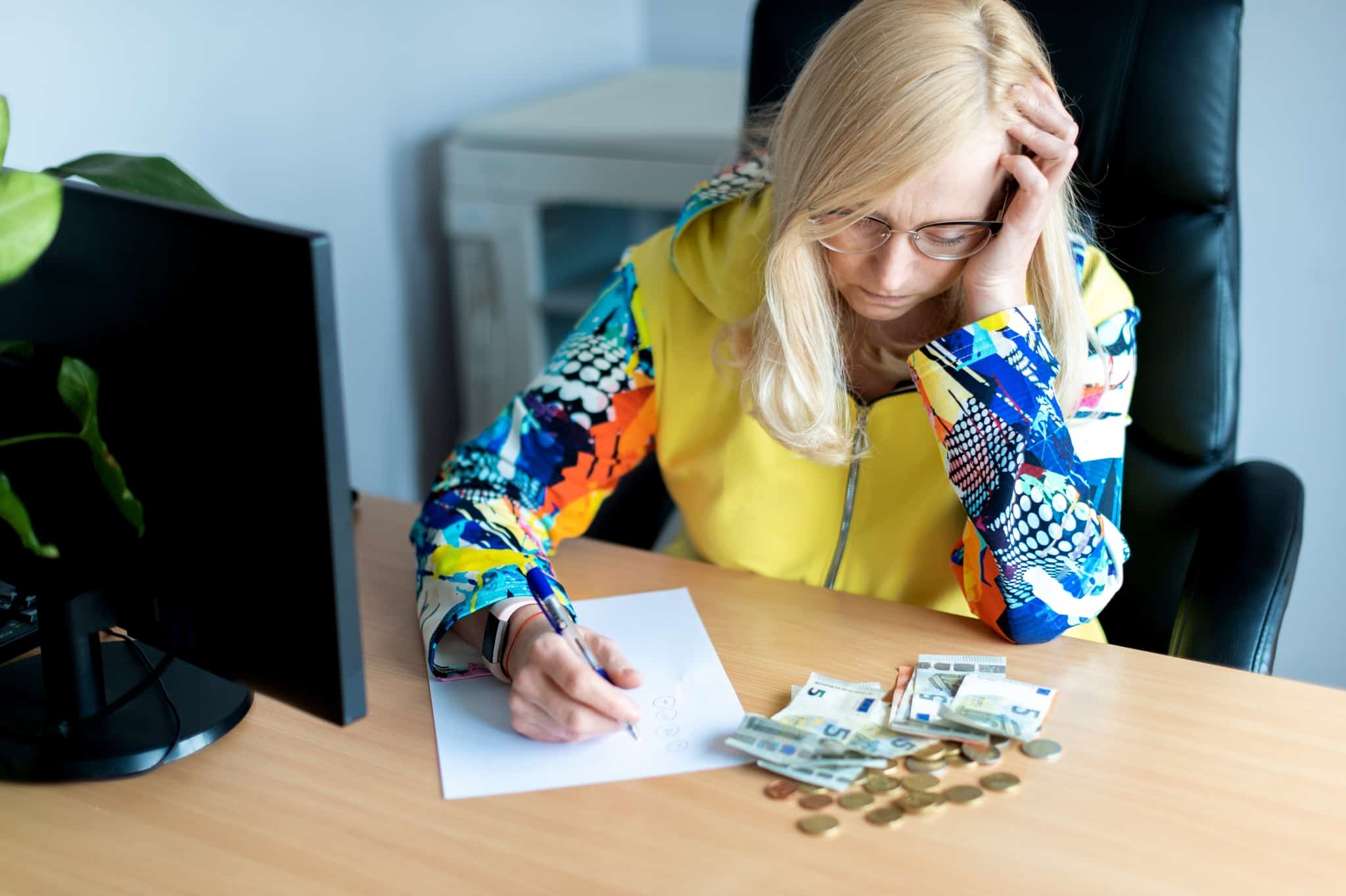 middle-aged woman with pencil and sheet of paper, sitting at the table where she has scattered coins and five euro notes, tries to make her budget relying only on irregular income