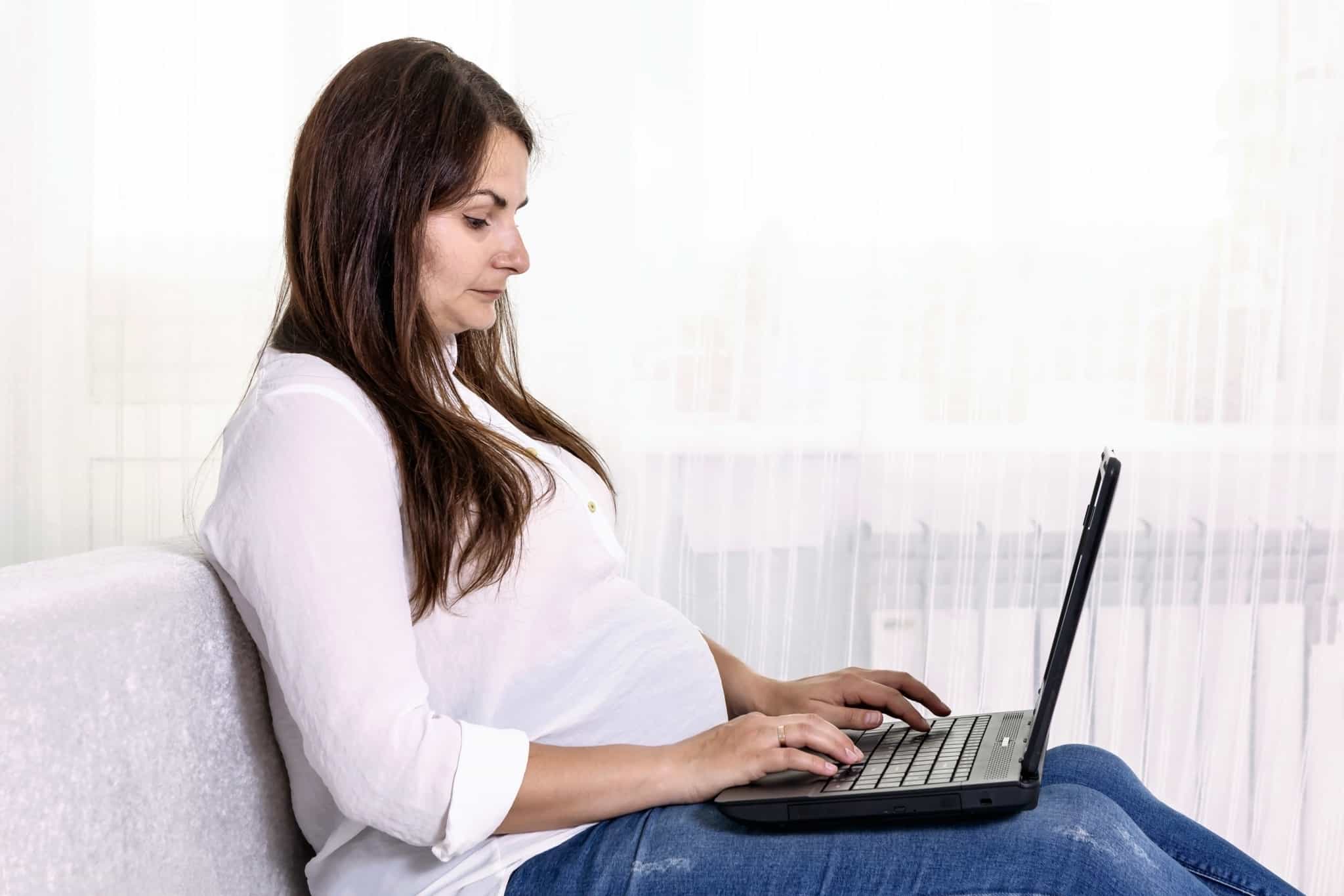 young pregnant woman messing around with her laptop on her lap