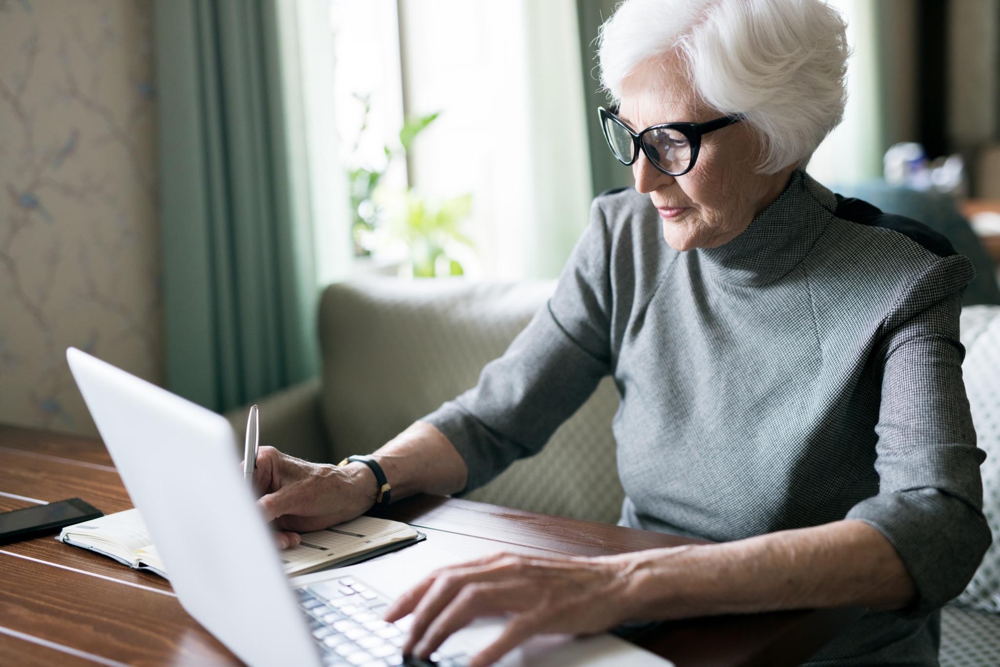Elderly woman writing in a notebook and consulting the computer