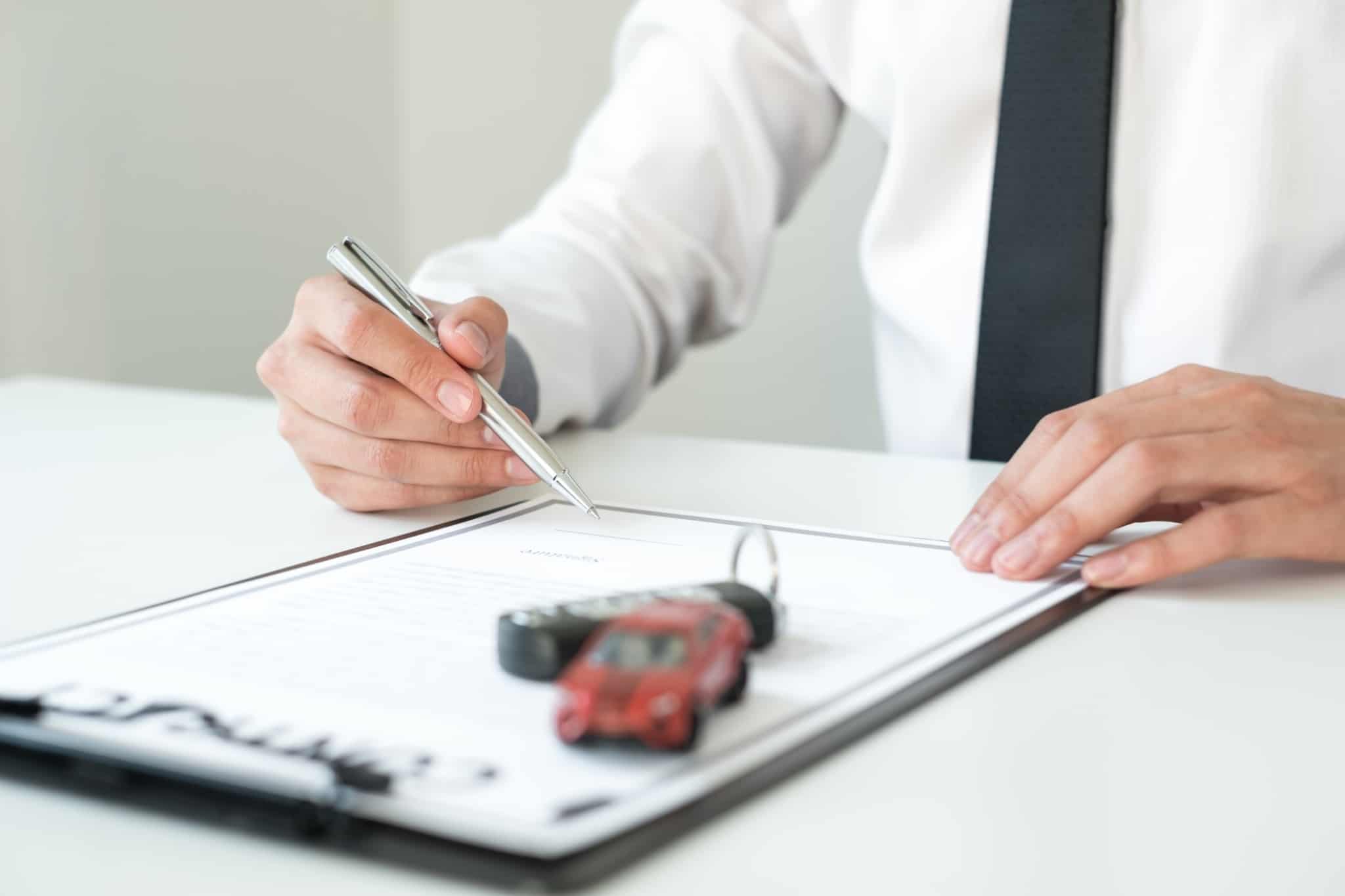 Image of a contract being signed by someone - on top of the contract is a miniature car and a key - credit intermediary