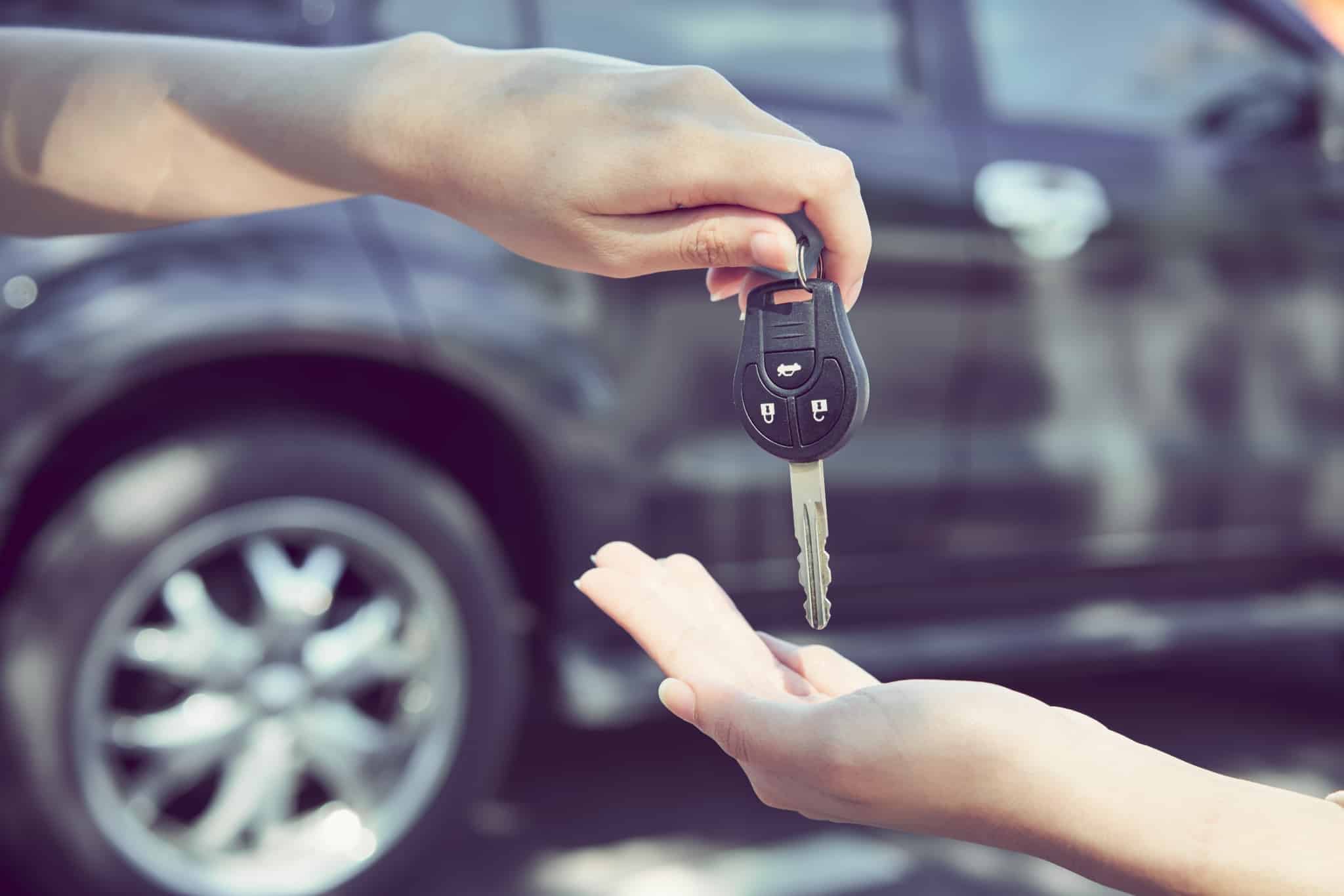 close-up of two hands with a car in the background, showing handing over keys and symbolizing the purchase of the vehicle.