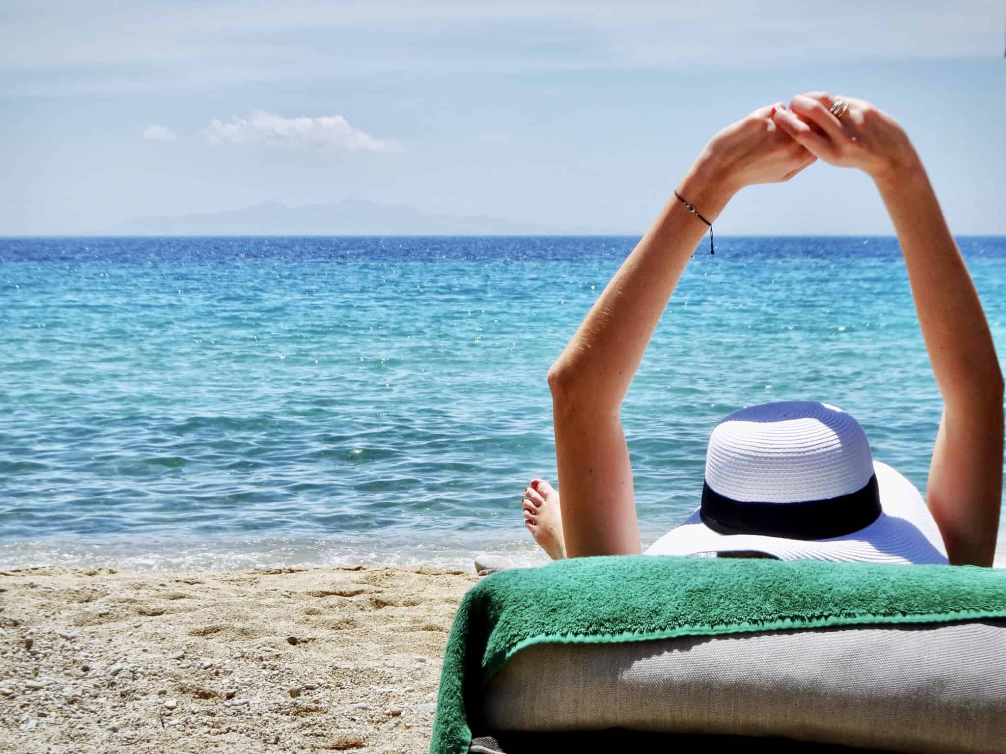 young woman sitting on a chair by the sea, with a white hat on her head, stretches and enjoys her vacation